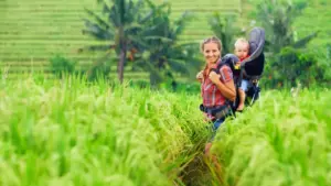 Jeune parent équipé d'un porte-bébé physiologique pour randonner avec un bébé sur un sentier de montagne en été.
