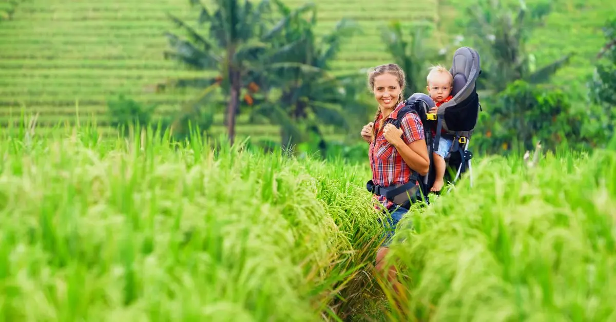 Jeune parent équipé d'un porte-bébé physiologique pour randonner avec un bébé sur un sentier de montagne en été.